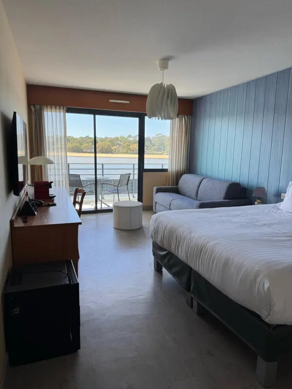Une chambre lumineuse avec un lit fait et un canapé face à une baie vitrée.