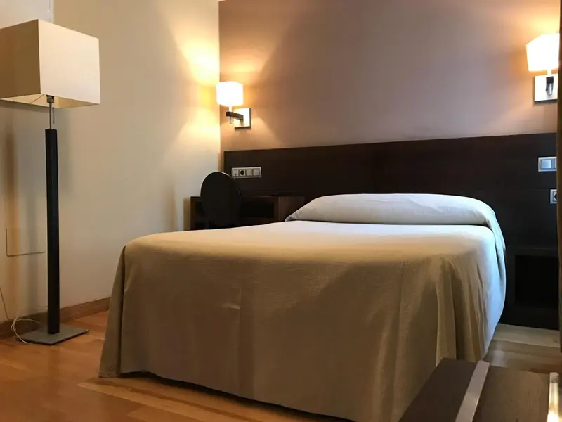 Une chambre avec un grand lit recouvert d'une couverture claire et un éclairage chaleureux.