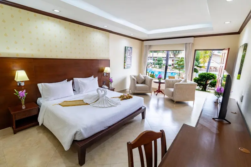 Chambre lumineuse avec un grand lit et un coin salon donnant sur une piscine.