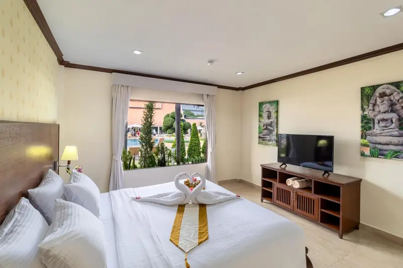 Chambre lumineuse avec un lit décoré de serviettes en forme de cygnes et vue sur une piscine.