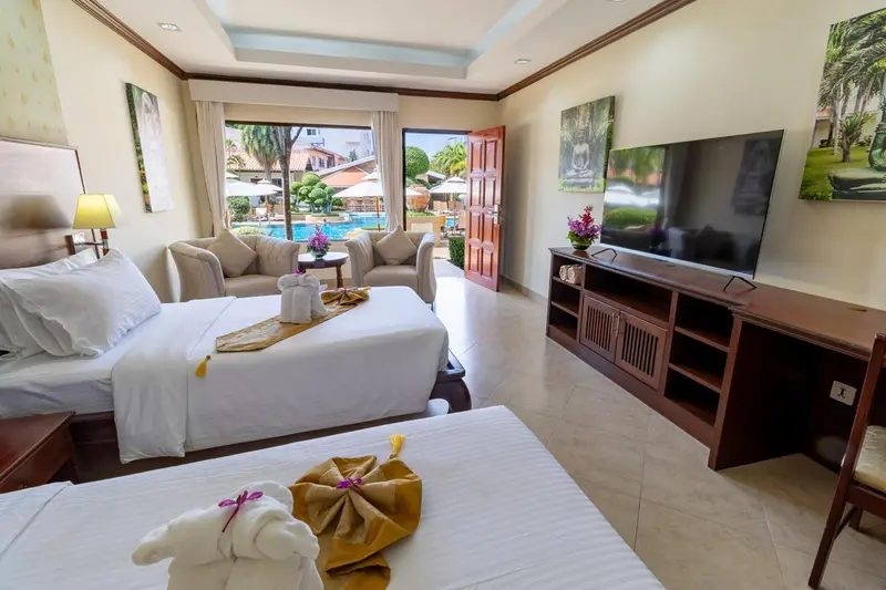 Chambre lumineuse avec un lit et un espace salon donnant sur une piscine.