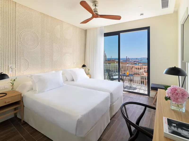 Chambre lumineuse avec un grand lit et un balcon donnant sur la mer.