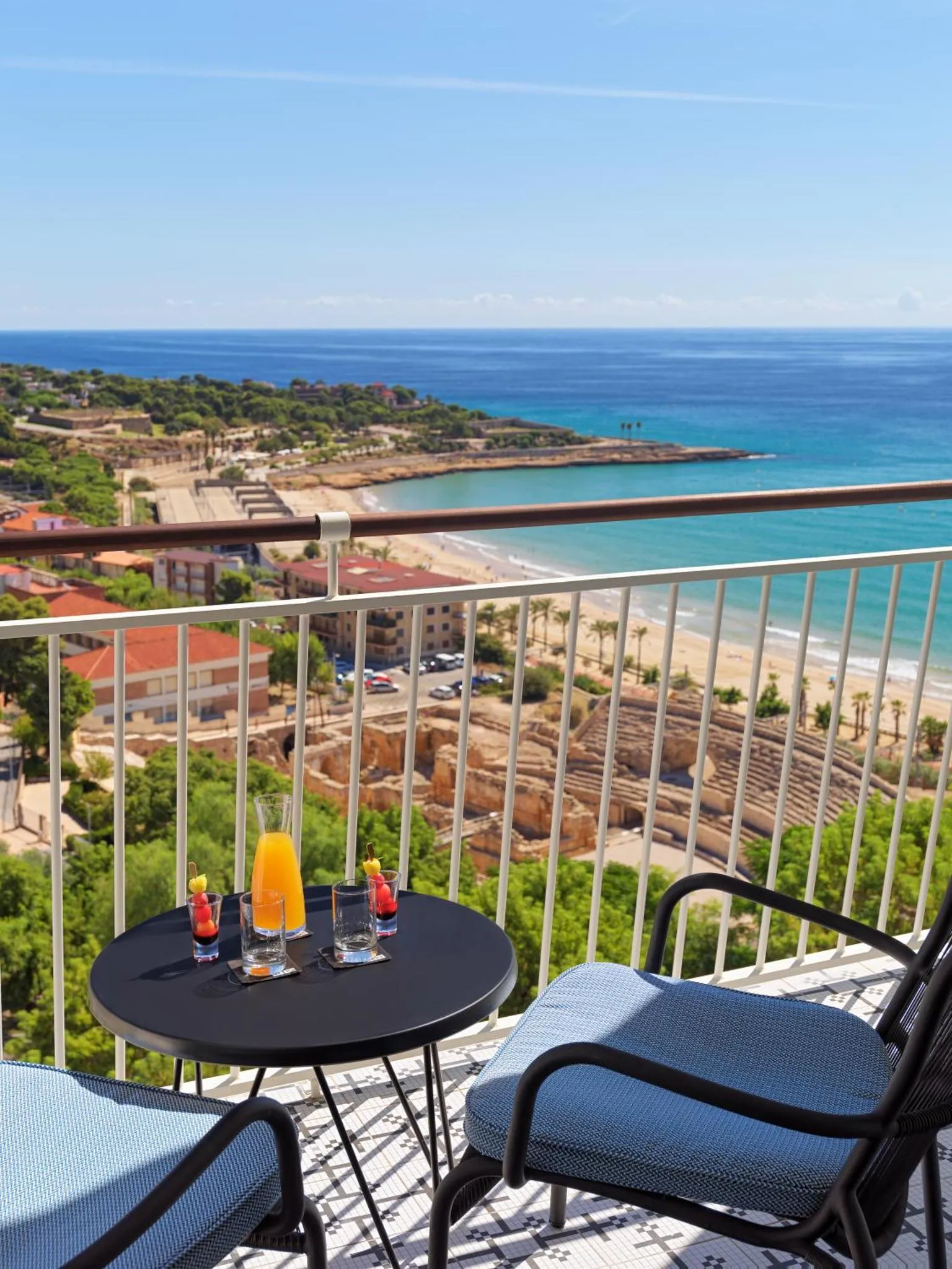 Une table basse avec des boissons est mise en scène sur une terrasse avec vue sur la mer et la côte.