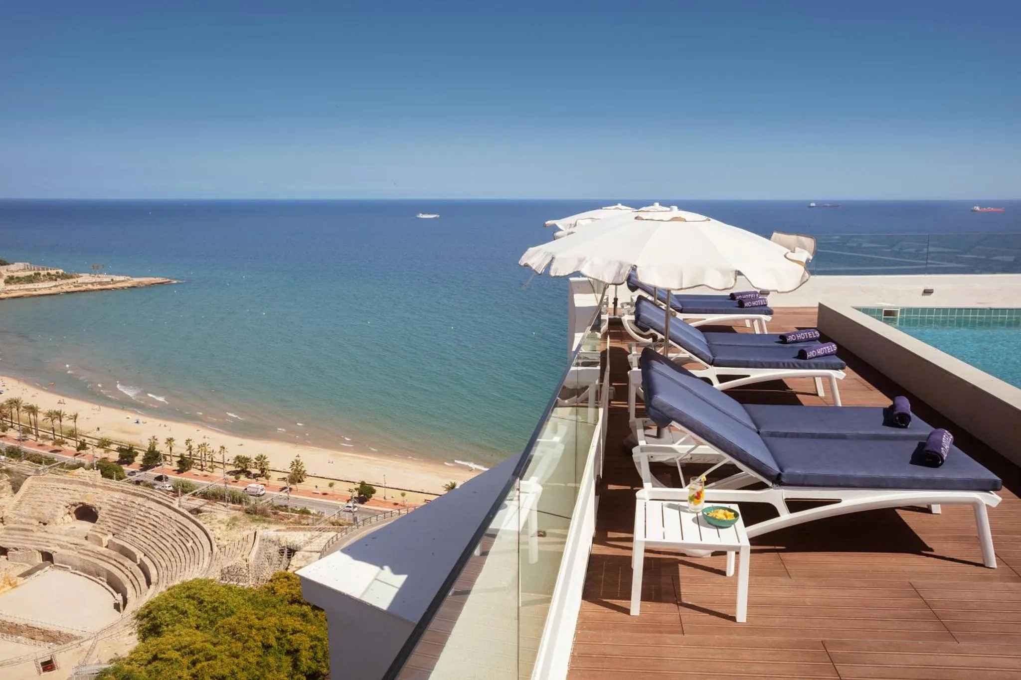 Terrasse avec transats blancs et parasols vue sur la mer et la plage.