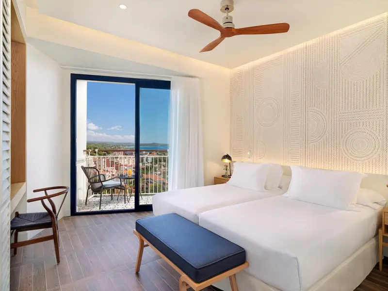 Chambre lumineuse avec un grand lit et un balcon offrant une vue sur la mer.