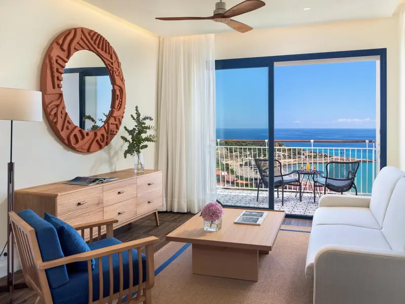 Une pièce lumineuse avec un canapé, une commode et un accès à un balcon avec vue sur la mer.