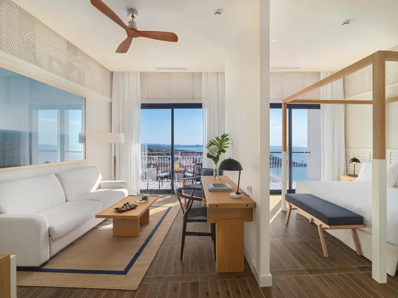 Une chambre lumineuse avec un canapé blanc et un lit à baldaquin donnant sur une vue mer.