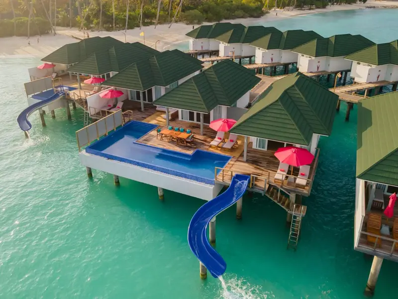 Vue aérienne de bungalows sur pilotis avec piscines et toboggans aquatiques.