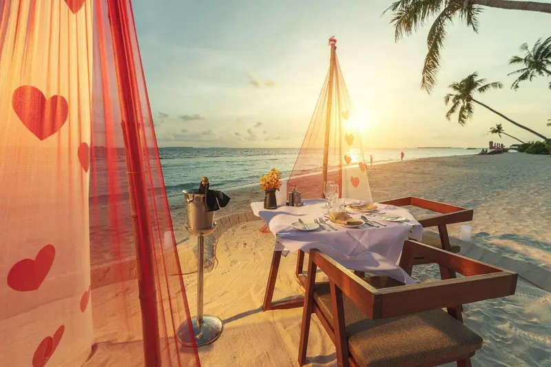 Table de dîner romantique dressée sur une plage au coucher du soleil.