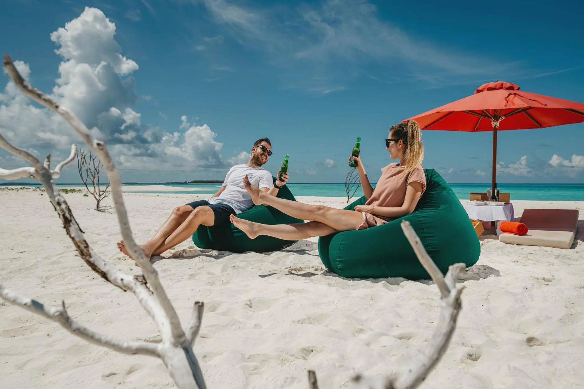 Deux personnes se détendent sur des fauteuils gonflables sur une plage de sable blanc.