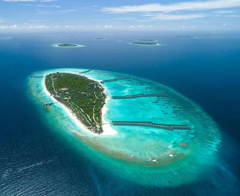 Vue aérienne d'une île tropicale entourée d'un lagon turquoise et de plages de sable blanc.