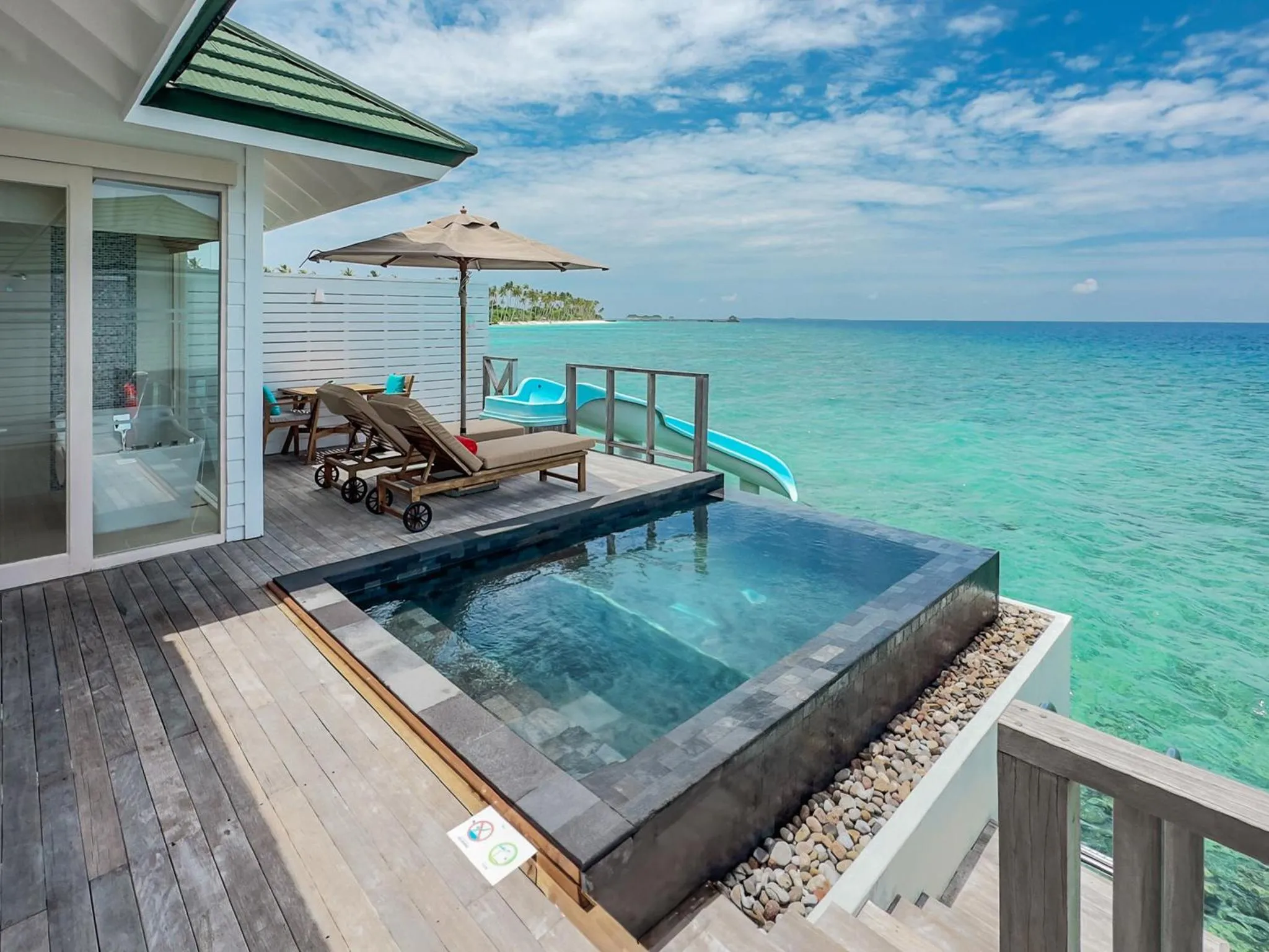 Terrasse en bois avec piscine et transats face à la mer turquoise.