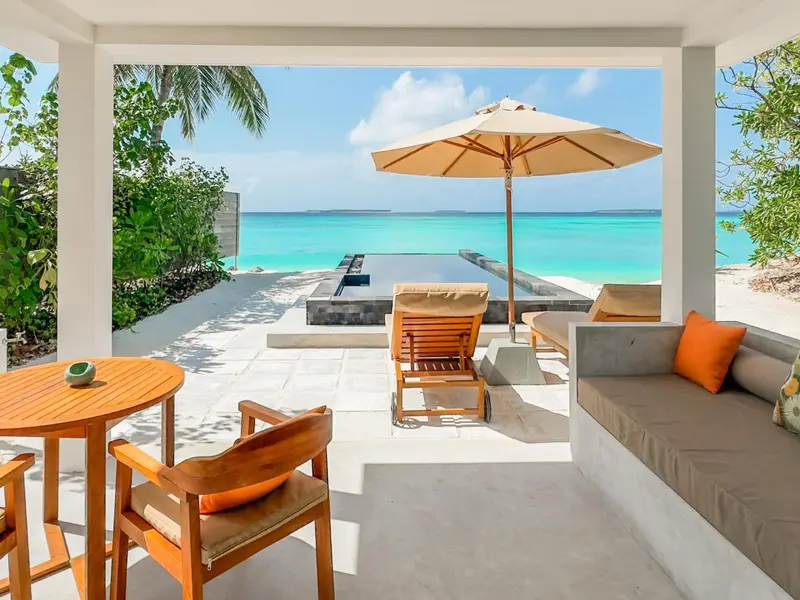 Terrasse avec mobilier de jardin et vue sur une plage turquoise.