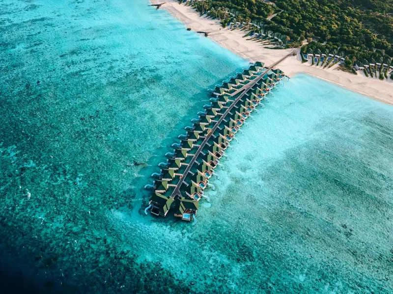 Vue aérienne d'une série de villas sur pilotis au-dessus d'un lagon turquoise.