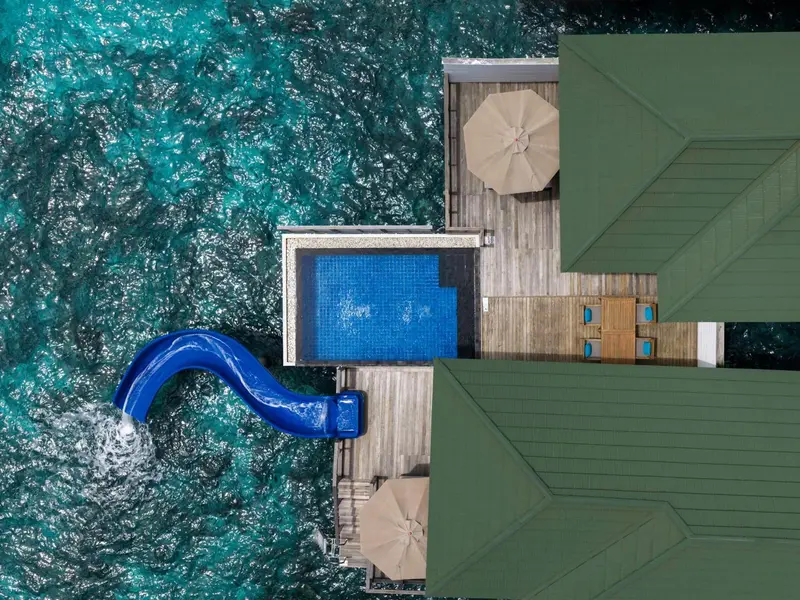 Vue aérienne de villas sur pilotis avec piscines et toboggan.