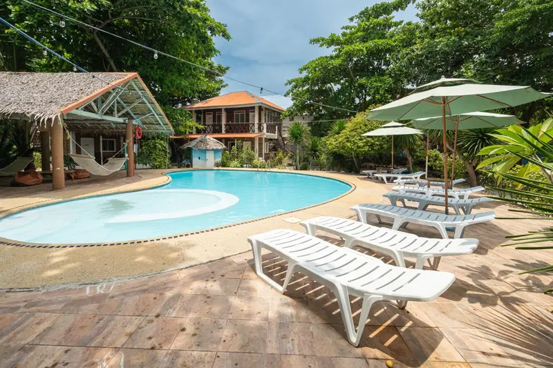 Transats blancs disposés autour d'une piscine turquoise dans un jardin tropical.