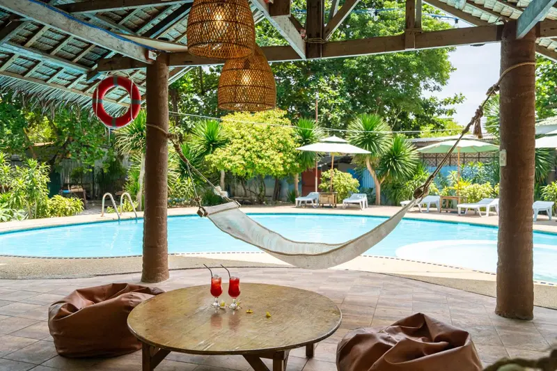 Un hamac est suspendu au-dessus d'une piscine, avec une table et des fauteuils à proximité.