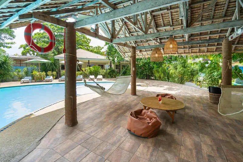 Espace de détente ombragé avec hamac et mobilier de jardin près d'une piscine.