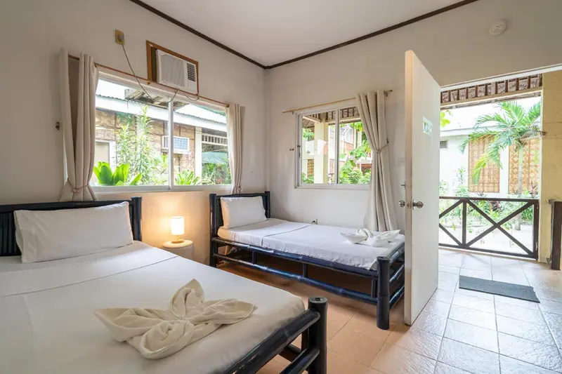 Chambre lumineuse avec deux lits simples et vue sur une végétation tropicale.