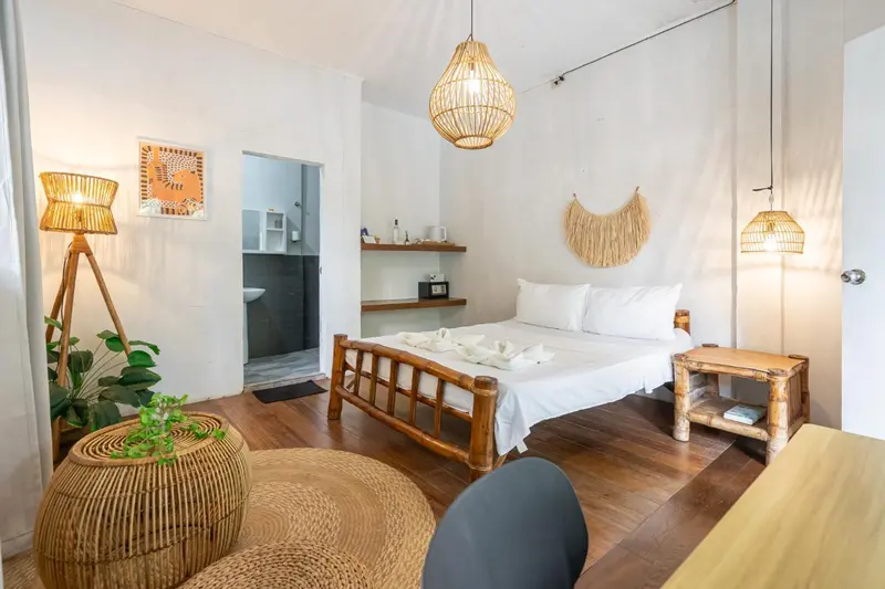 Une chambre lumineuse avec un lit recouvert de blanc et des éléments en rotin.