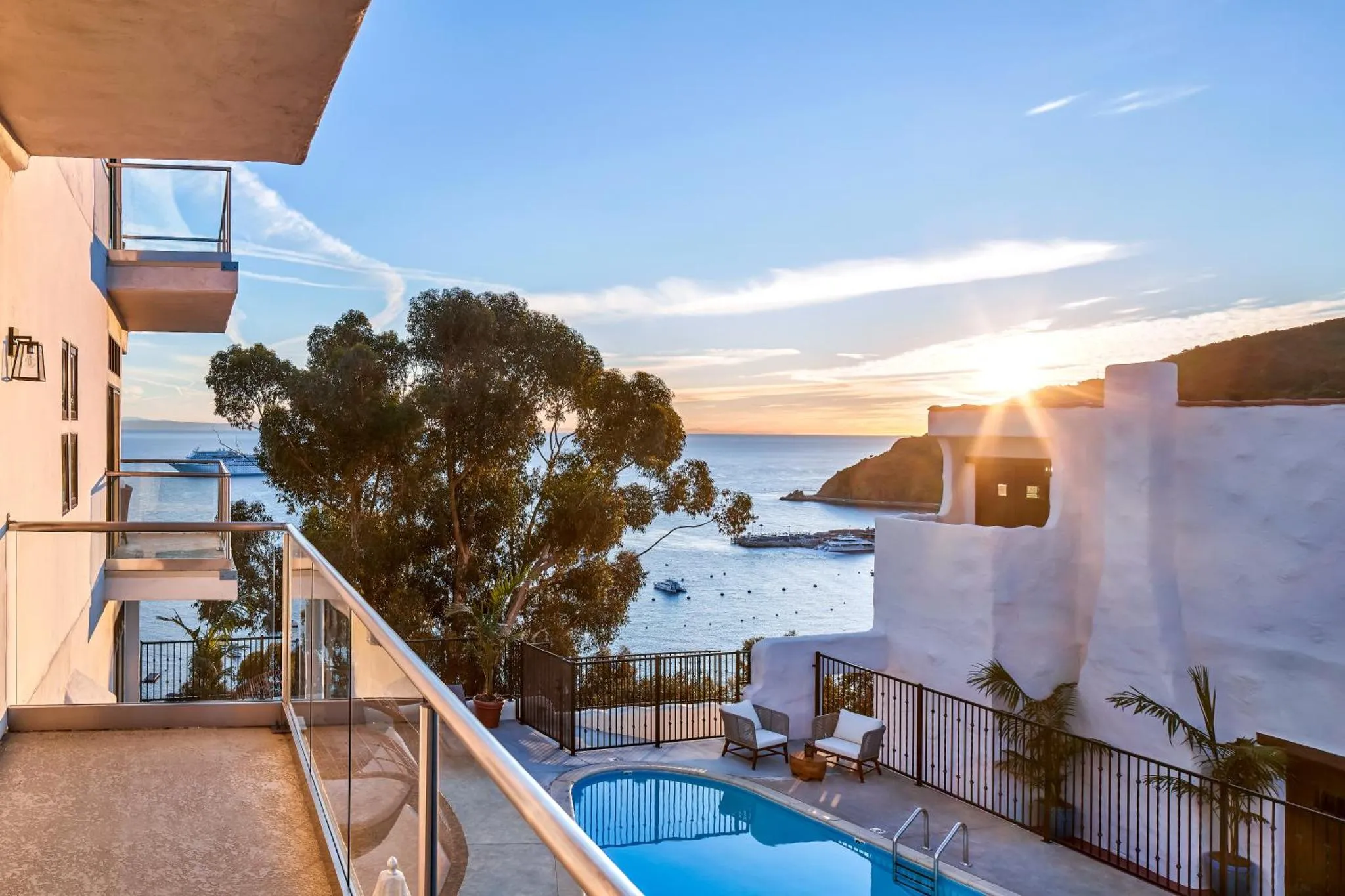 Vue d'une terrasse avec piscine donnant sur la mer au coucher du soleil.