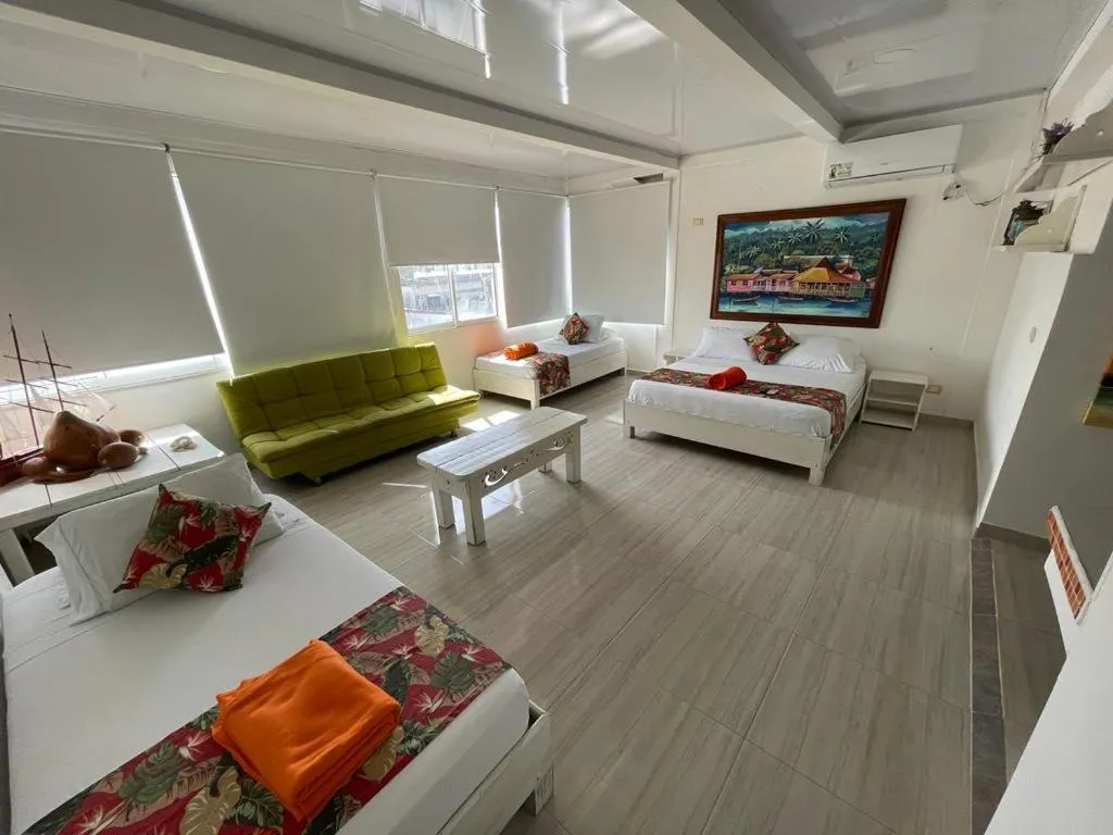 Espace de vie lumineux avec canapés verts et lits décorés de coussins colorés.