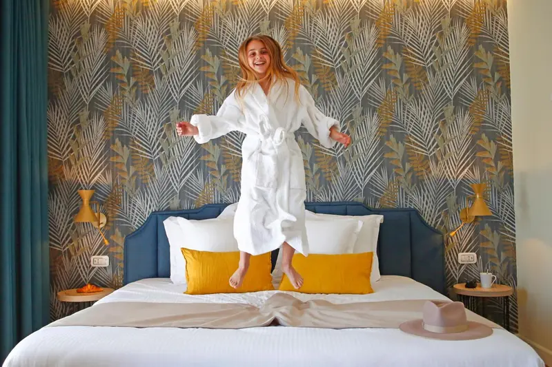 Une jeune femme saute de joie sur un grand lit dans une chambre décorée.