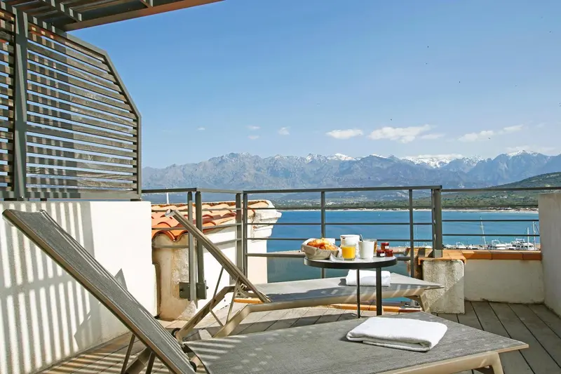 Terrasse avec transats et table basse face à la mer et aux montagnes.
