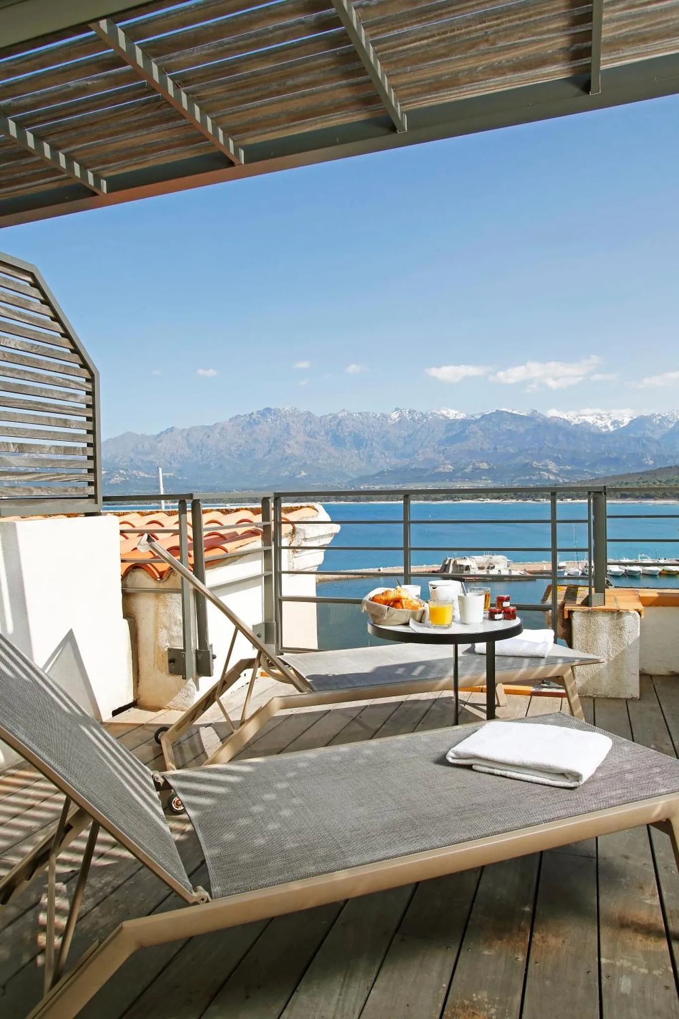 Terrasse en bois avec transat et table basse donnant sur la mer et les montagnes.