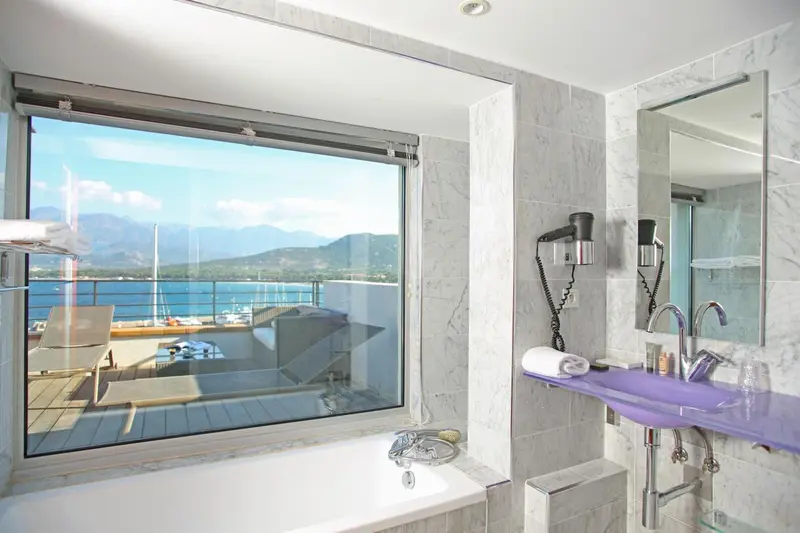 Une salle de bain lumineuse avec baignoire et vue sur la mer.