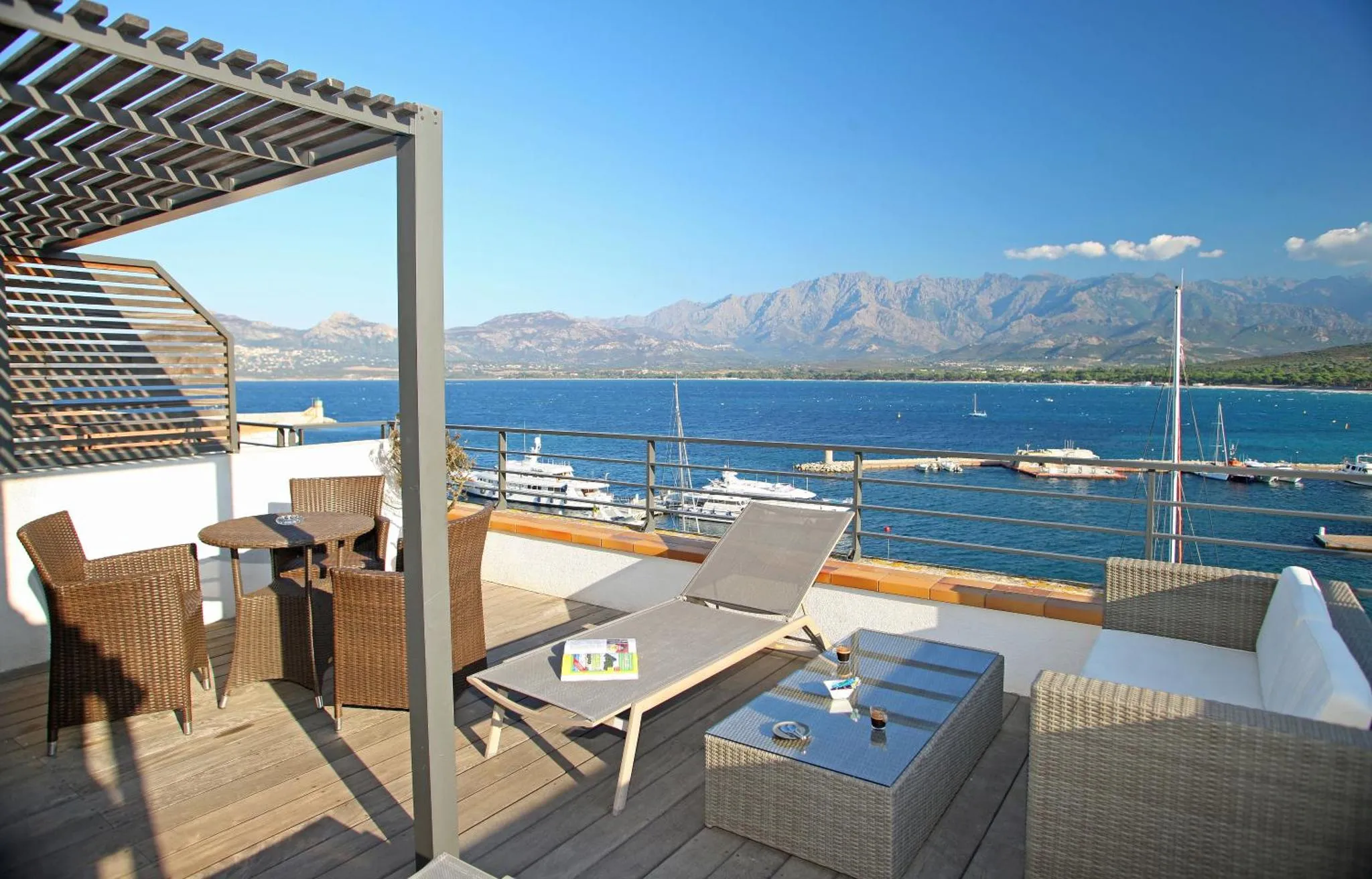 Terrasse aménagée avec mobilier de jardin et vue sur la mer et les montagnes.