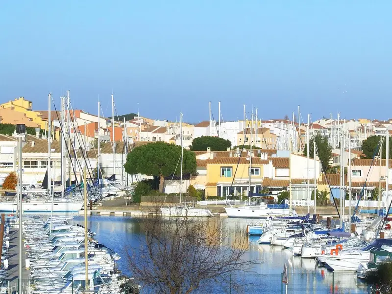 Vue d'un port de plaisance ensoleillé avec des bateaux amarrés et des bâtiments en arrière-plan.