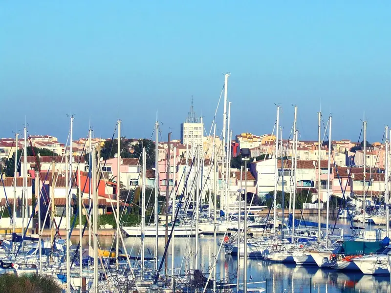 Port de plaisance ensoleillé avec de nombreux bateaux à mâts hauts.