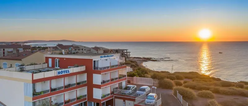Bâtiment rouge et blanc avec des balcons surplombant une côte rocheuse au coucher du soleil.