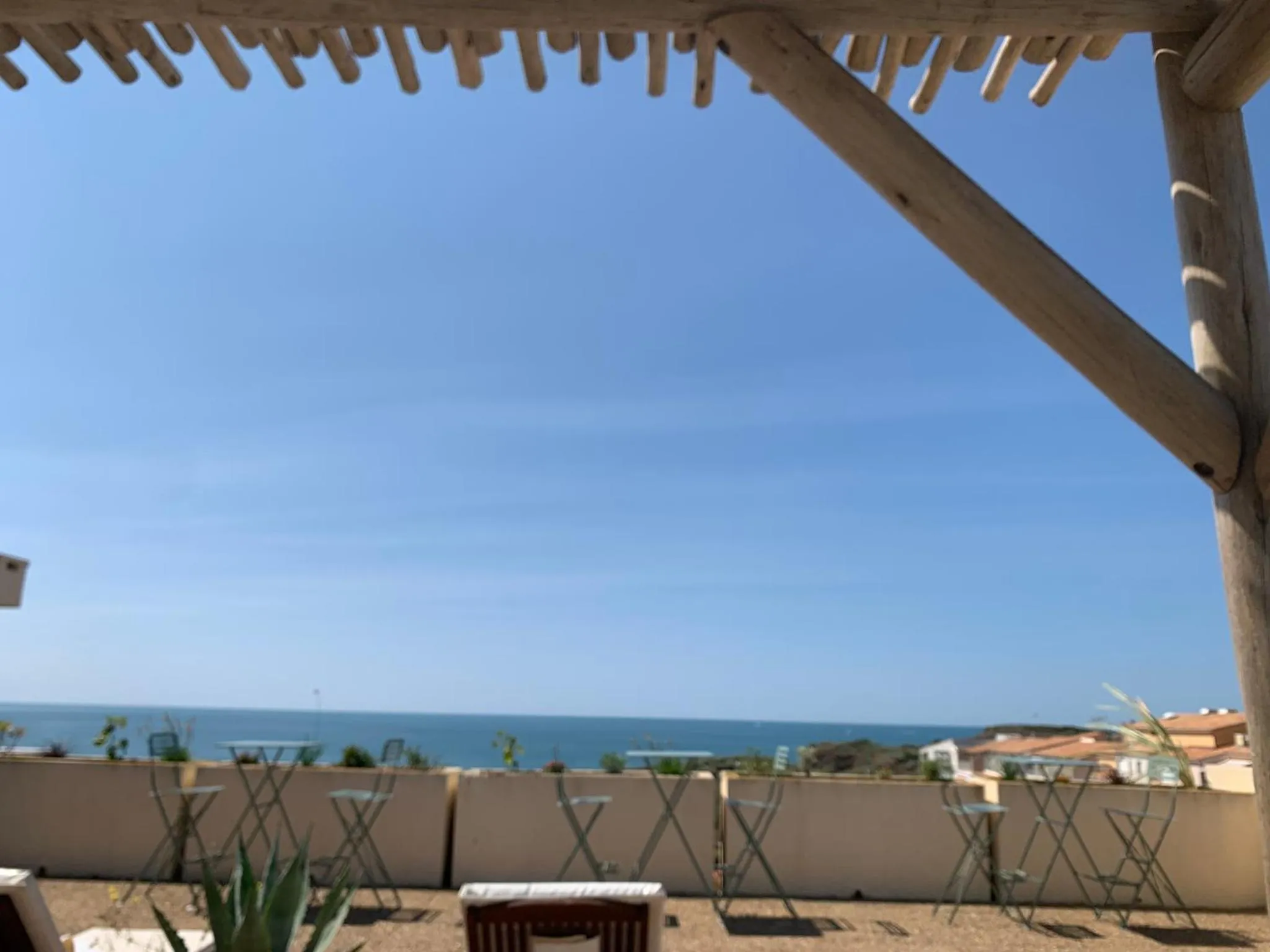Terrasse ombragée donnant sur la mer et une côte rocheuse.