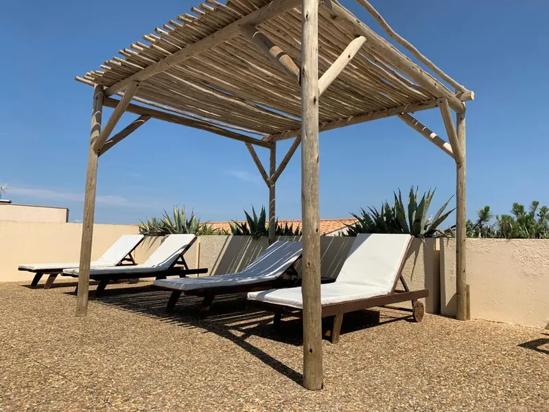 Transats blancs sous une pergola en bois sur une terrasse en gravier.