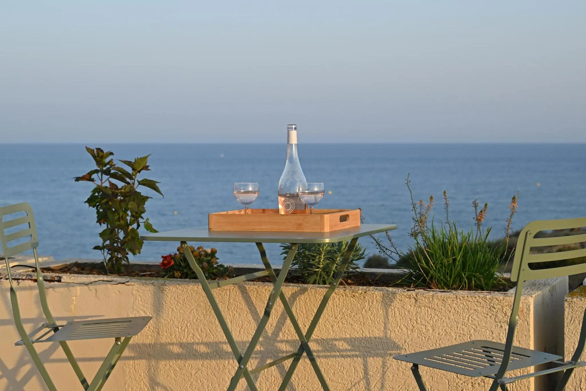 Une table avec des verres et une bouteille est posée sur une terrasse avec vue sur la mer.