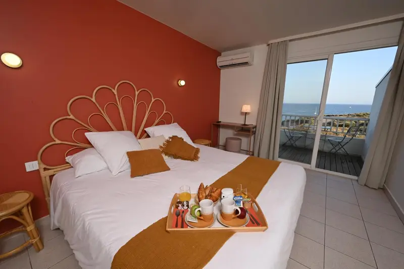Une chambre avec un petit-déjeuner servi sur le lit, donnant sur une terrasse et la mer.