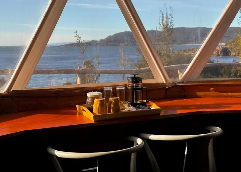 Une table en bois avec un service à café est placée devant une grande fenêtre donnant sur la mer.