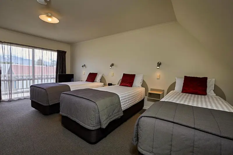Chambre avec trois lits simples et vue sur un paysage montagneux.
