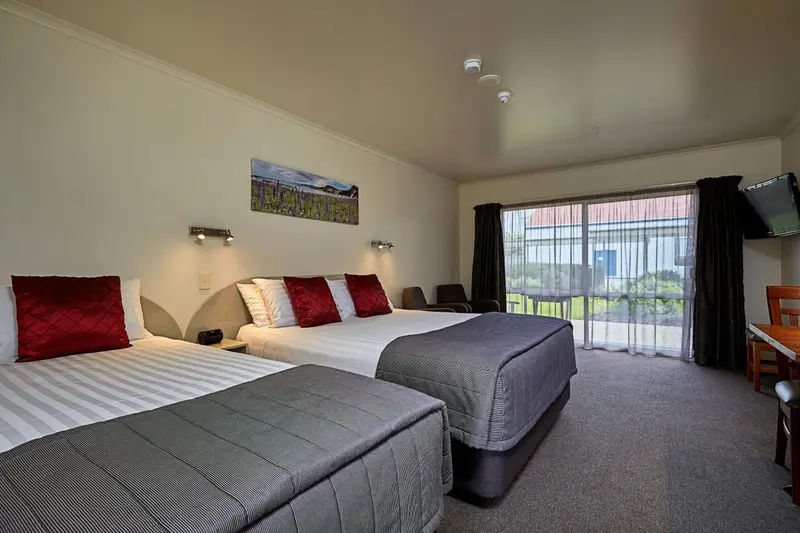 Une chambre lumineuse avec deux lits et un coin repas près d'une baie vitrée.
