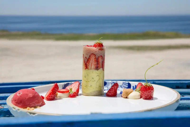 Un dessert à la fraise est présenté sur une assiette décorée, avec la mer en arrière-plan.