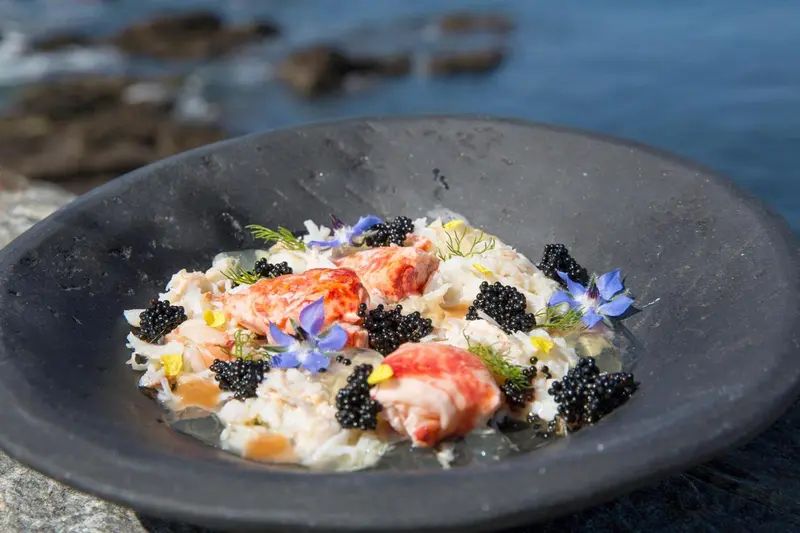 Un plat de fruits de mer est présenté dans un bol noir sur un rocher face à la mer.
