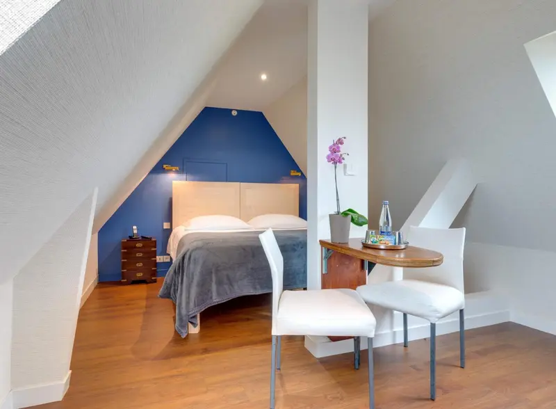 Une chambre mansardée lumineuse avec un lit double et une petite table.