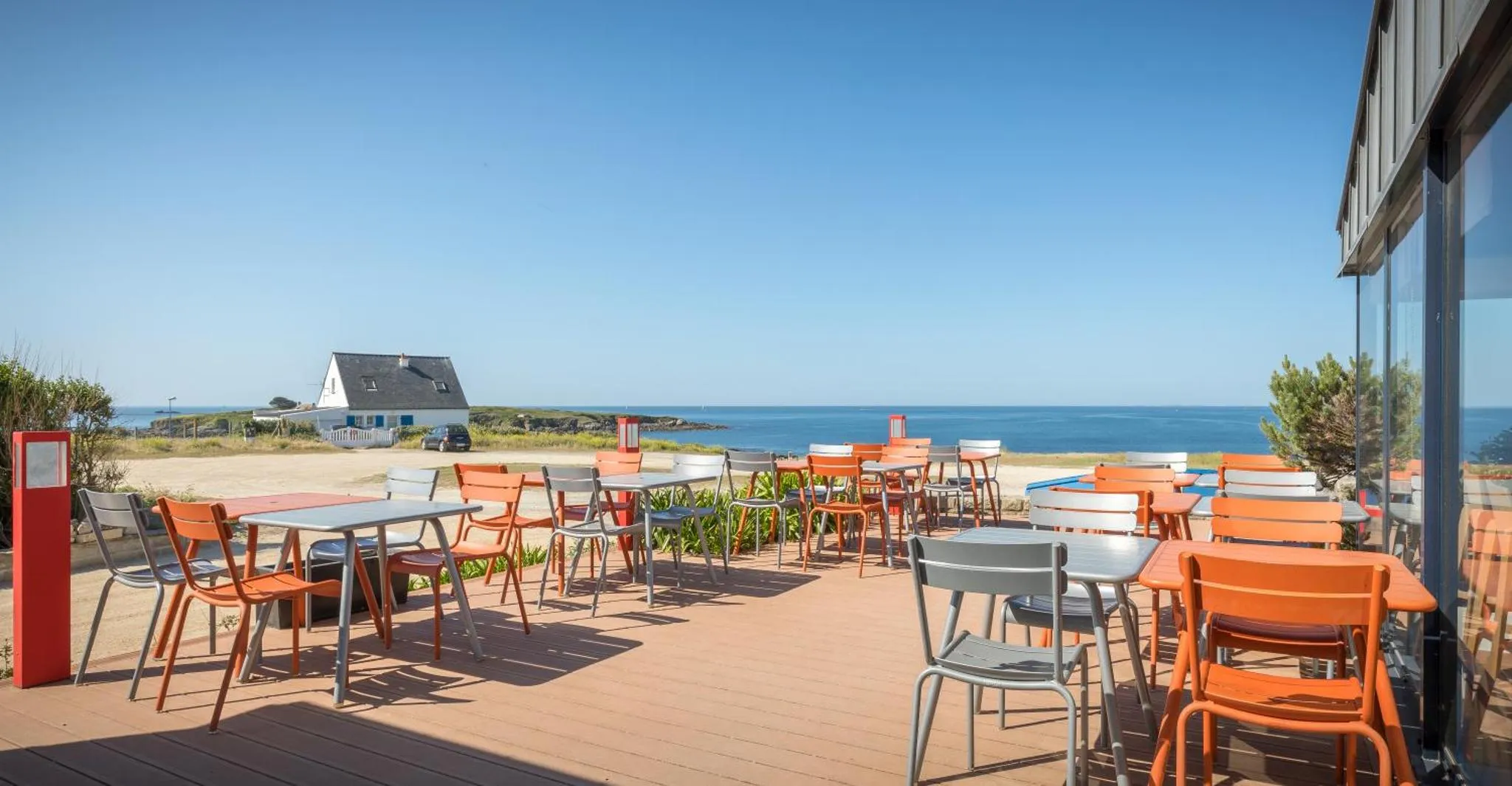 Terrasse ensoleillée avec tables et chaises face à la mer.
