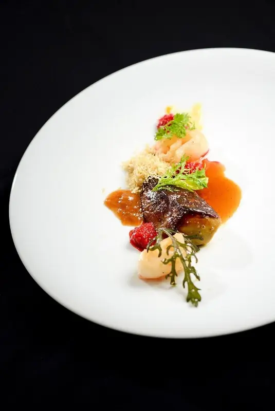 Assiette raffinée ornée de fruits de mer et de sauces colorées.