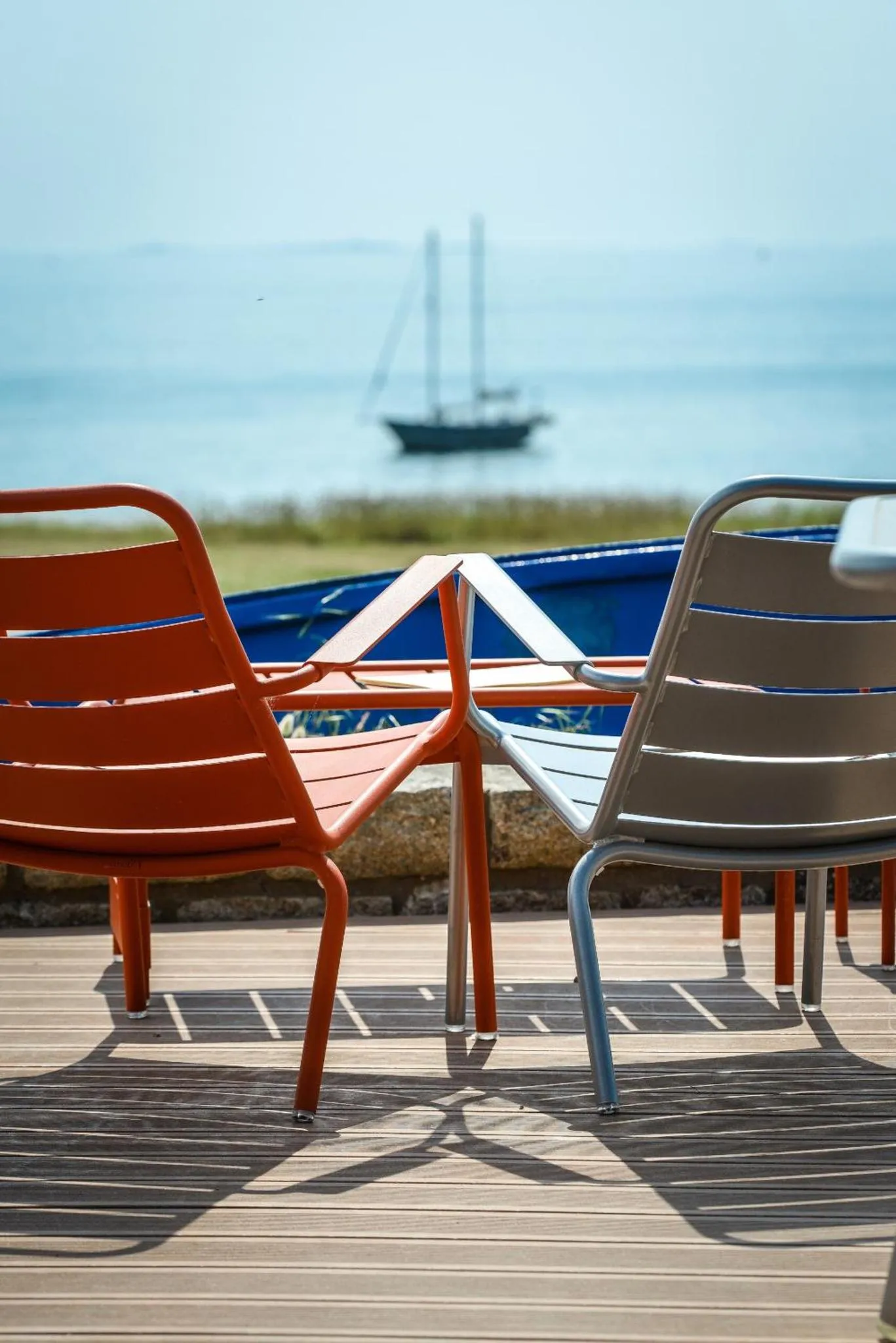 Chaises colorées sur une terrasse en bois face à la mer.
