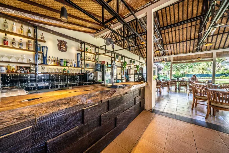 Un long comptoir en bois sombre est aligné de bouteilles, devant un espace de restauration extérieur.