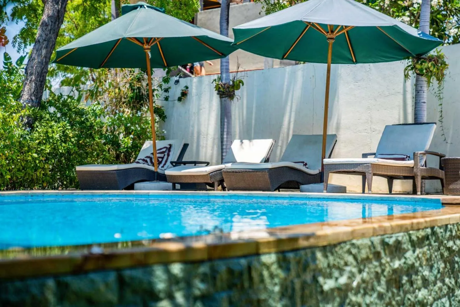 Transats et parasols ombragent une piscine turquoise bordée de verdure.