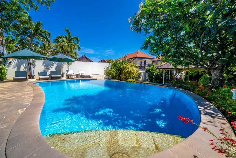 Piscine bleue entourée d'une terrasse ensoleillée et d'une végétation luxuriante.